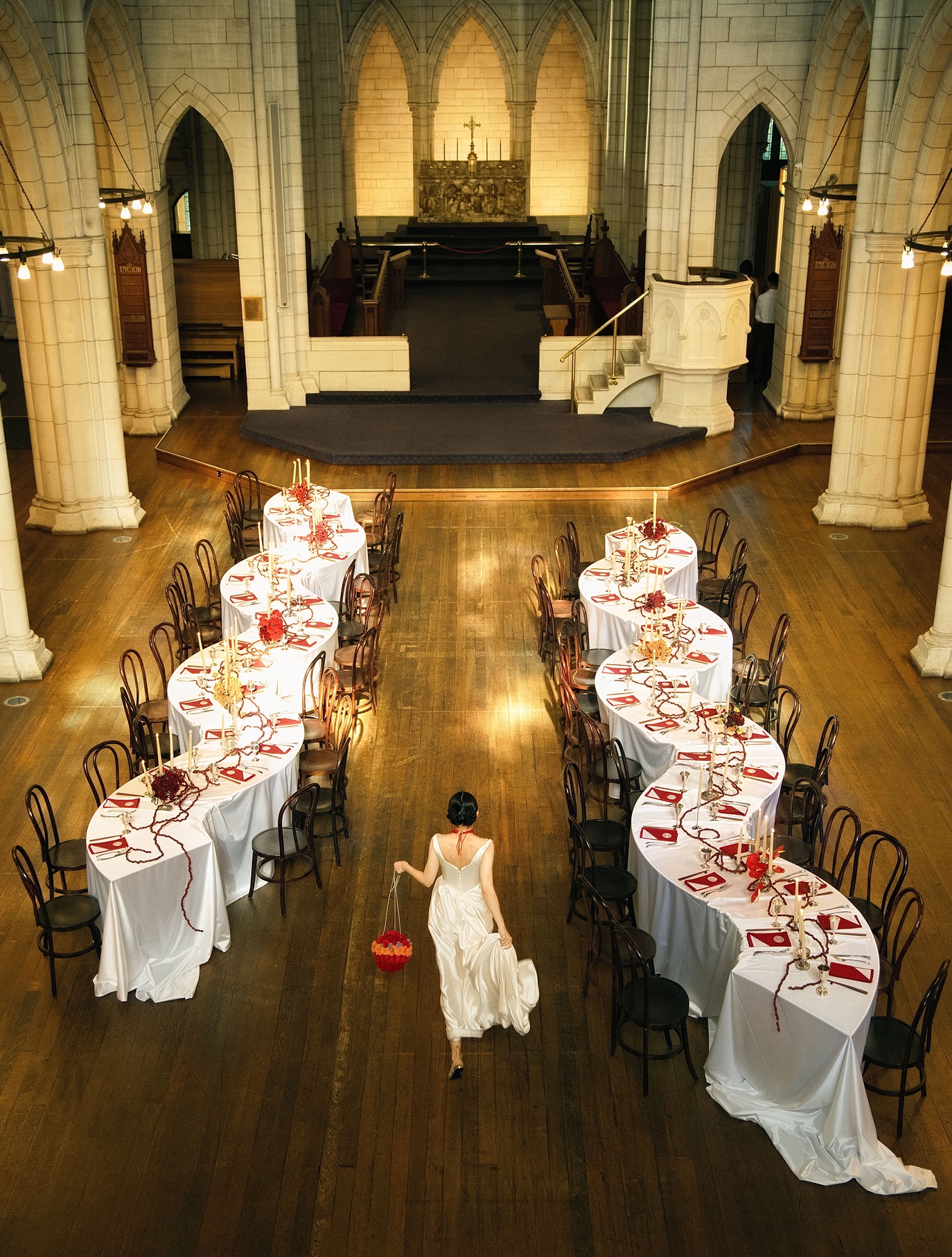 A church laid with serpentine banquet tables in white and red, a bride walking between them