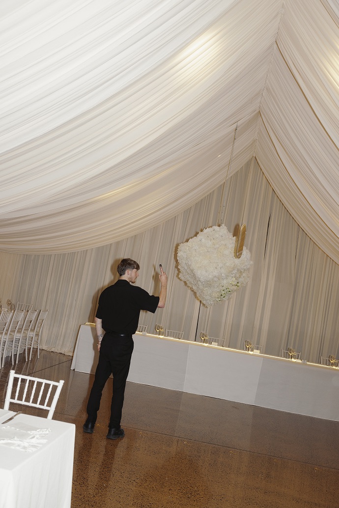 A florist fixing a white floral installation to the draped wall of a marquee