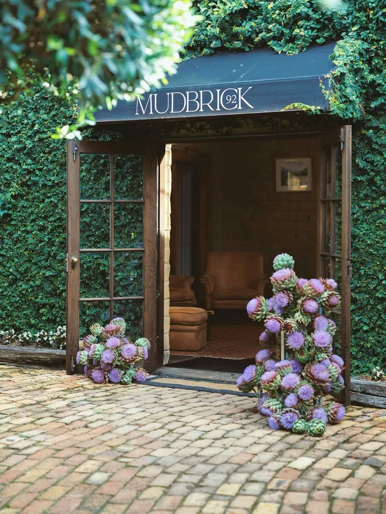The ivy-covered entrance to Mudbrick, flanked by purple artichoke thistles
