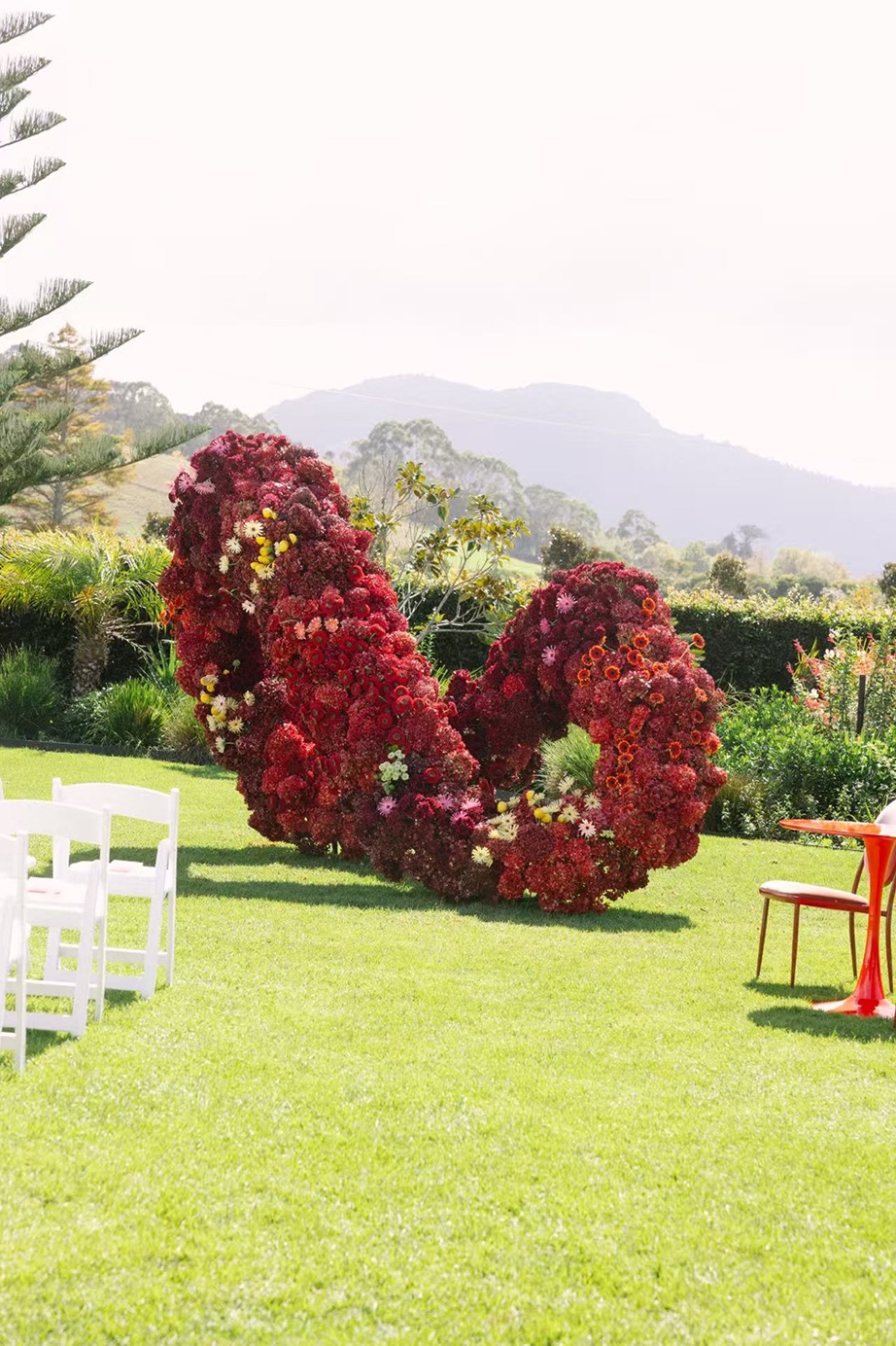 A sculptural arch of deep red blooms standing on a lawn